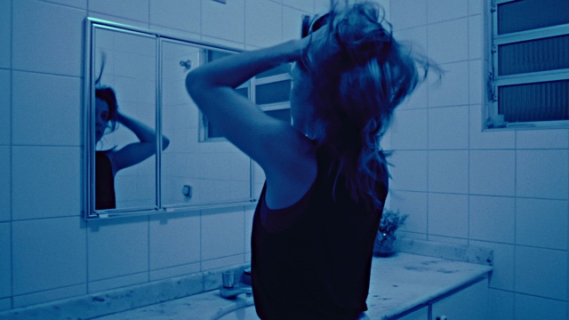 a woman faces a bathroom mirror and tussles her hair