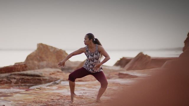 a dancer surrounded by red and brown rock looks and reaches to the side