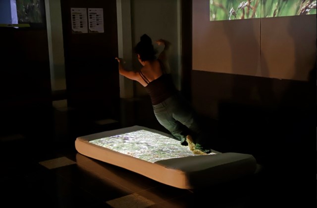a woman leaps sideways onto a mattress with a dance film projected onto it