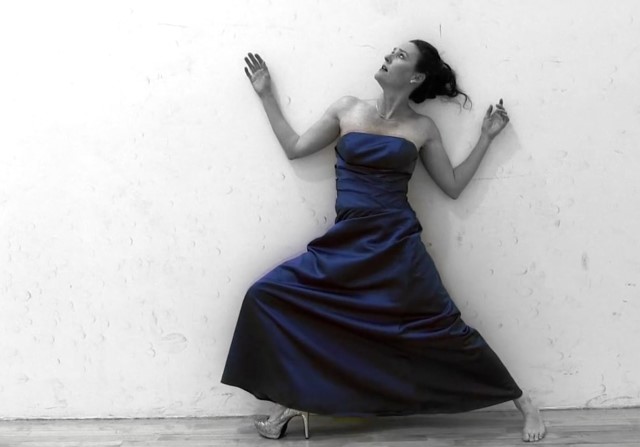 a woman in a blue ball gown presses her back against a wall; the rest of the photo is colorless