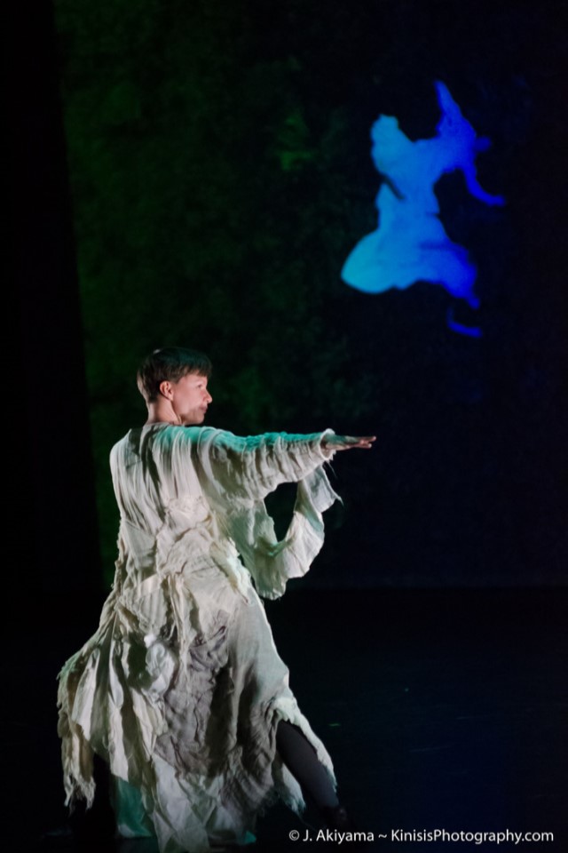 a short haired woman in a tattered white dress looks behind her with right arm outstretched