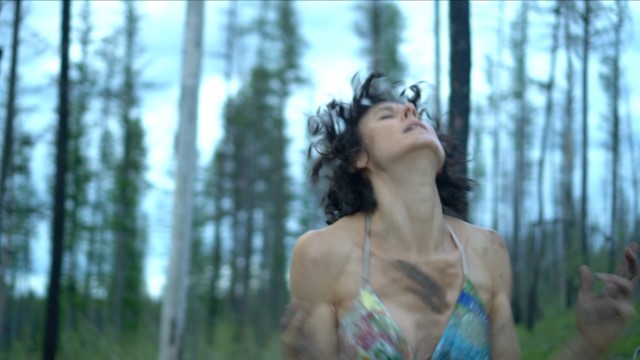 a light skinned woman in a forest leans her head back; the image is blurry from her motion