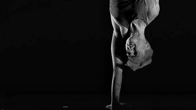 an aerial dancer balances on one hand in front of a black background