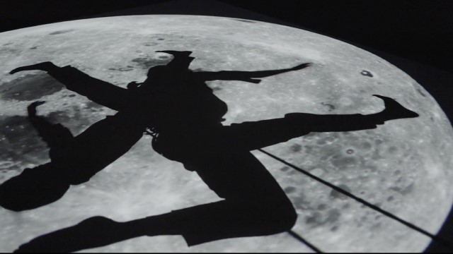 silhouettes of two aerial dancers punctuate a projection of the moon