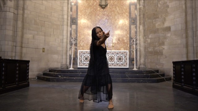 a dark skinned woman dances alone in a small church, facing the camera