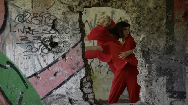 two dancers wearing bright red dance in an abandoned brick building with graffiti on the walls