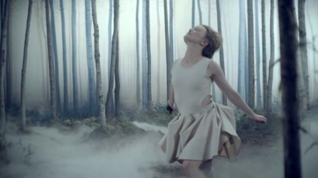 a dancer in a short cream colored dress runs through a misty forest, eyes closed and head tilted back