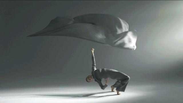 a dancer in loose grey clothing bends fully backward with only her toes on the ground; a large white sheet floats above her