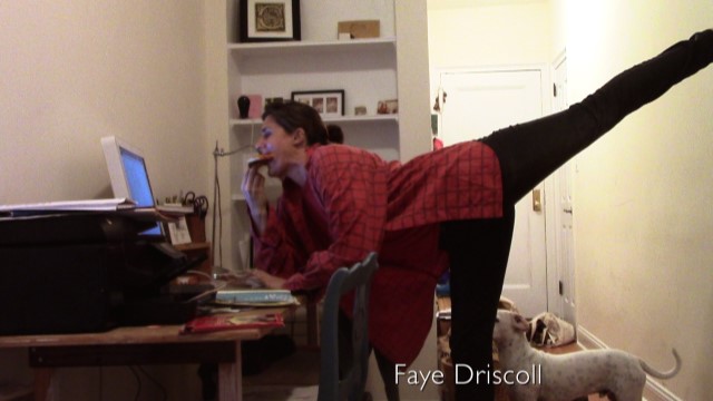 a dancer eating pizza leans forward, right leg extended behind her, to look at her computer monitor