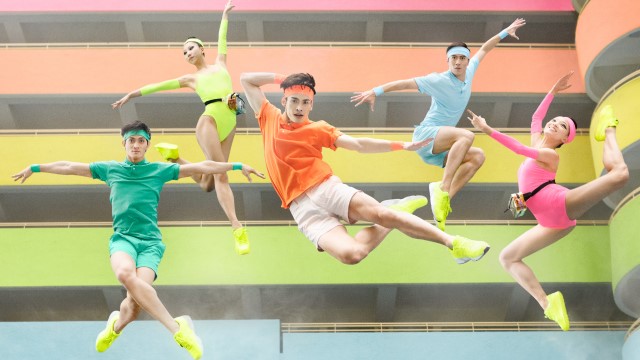 ballet dancers in neon-colored clothing and sneakers leap high in the air