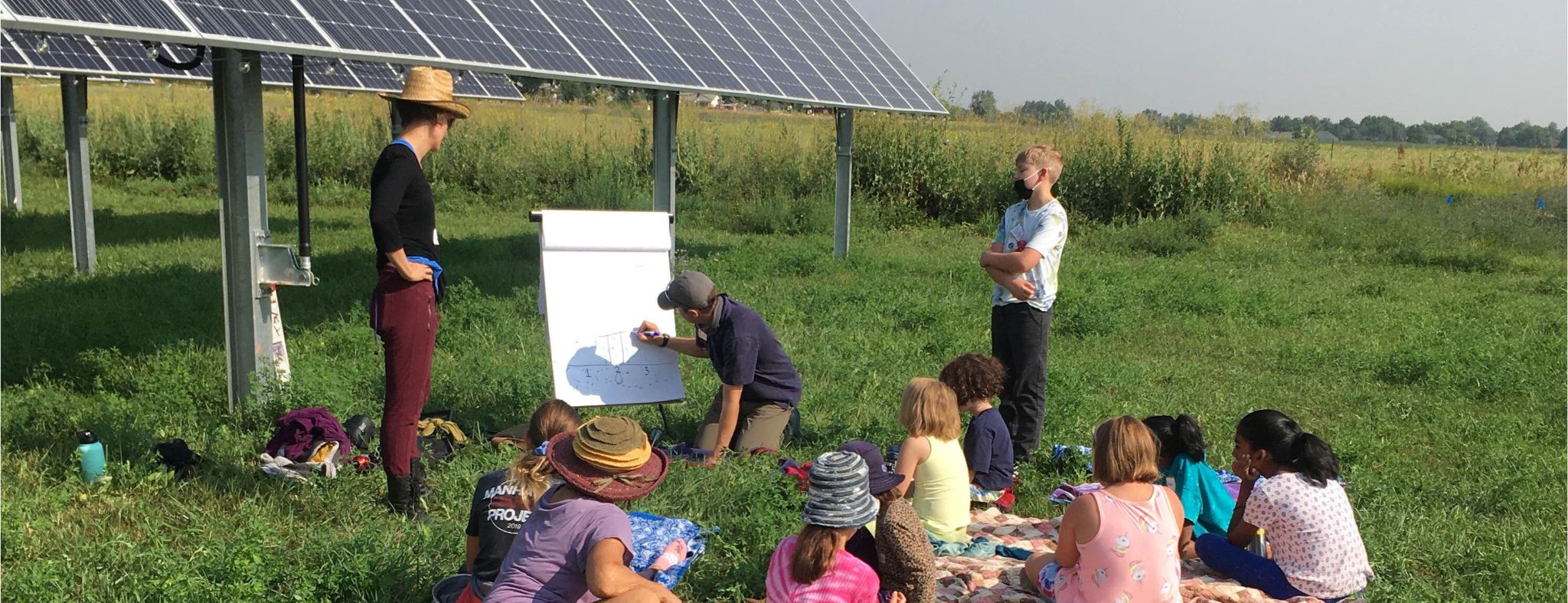 two adults demonstrate filmmaking storyboarding to children at a dance film workshop on a working solar farm