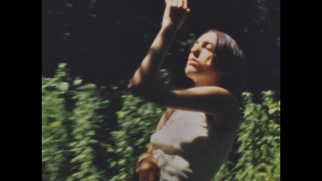 a washed out image of a woman with short brown hair dancing in front of a vine-covered wall