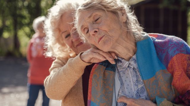 an older woman leans her head comfortably on the hand of a childhood friend