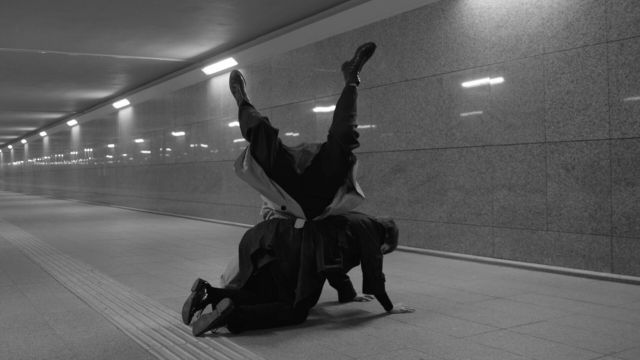 a black and white photo of a person on their hands and knees with another person leaning on them, feet in the air