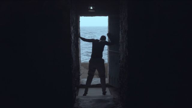 a man's silhouette stands in a stone doorway, facing away from the camera and out toward the ocean