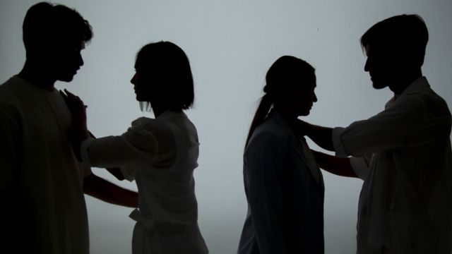 silhouetted, two pairs of dancers face each other with hands on each other's shoulders