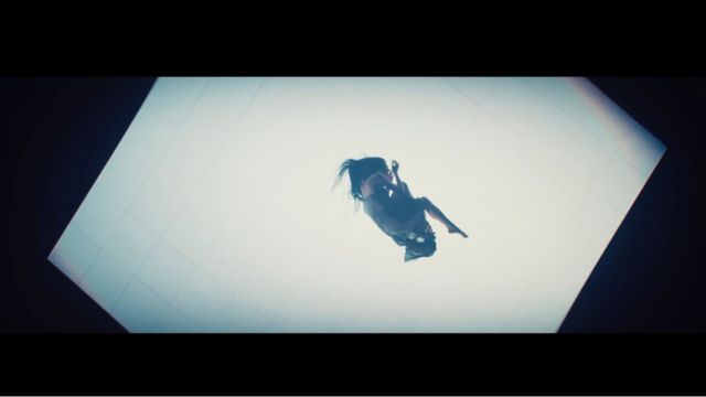 an overhead shot of a woman lying on her side on an illuminated section of floor in an otherwise dark room