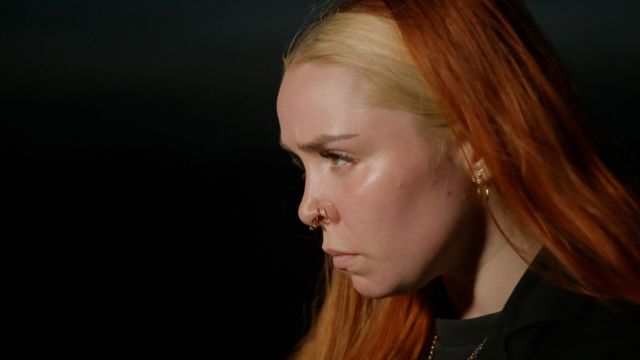 a closeup of the face of a young light skinned woman with red hair, looking intently toward the left edge of the frame