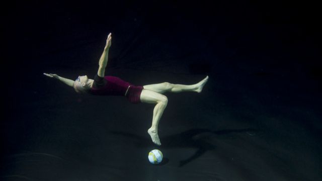 underwater, a soccer player is flailing, having just missed an attempt to kick a soccer ball