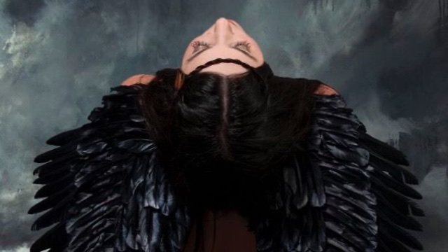 from directly above, we see a woman wearing a garment of black crow feathers tilting her head back slightly