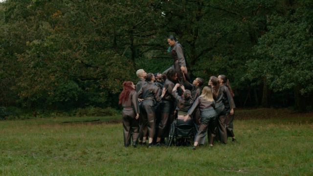 a single dancer stands atop a crowd of ten or more dancers who are supporting his weight