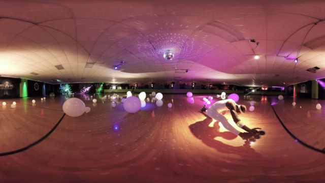 a dark skinned man doing the splits on roller skates in a bowling alley; the image's perspective is distorted because it is intended to be viewed in a 360-degree virtual reality headset