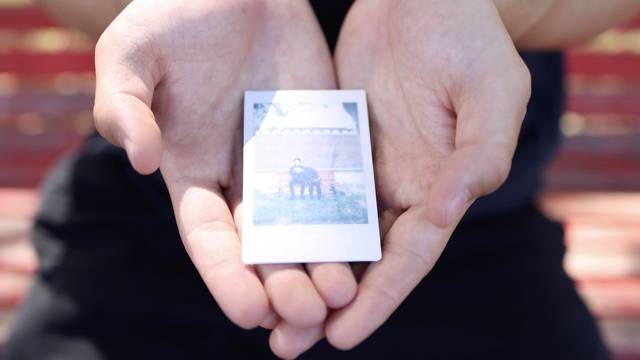 a closeup of a pair of light skinned hands holding a small piece of paper, the size of a playing card, with a photo on it