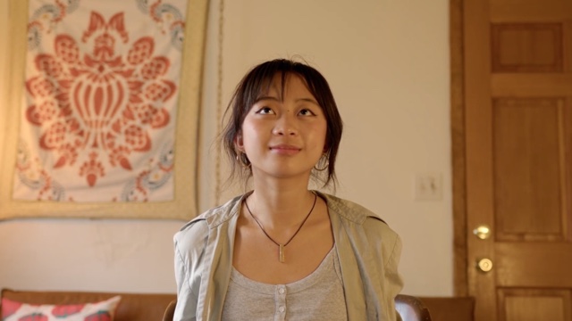 an Asian woman smiles slightly in a room, eyes looking toward the ceiling