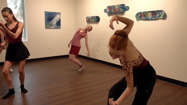 three young girls contort their bodies in an indoor art exhibit with several colorful pieces affixed to the walls