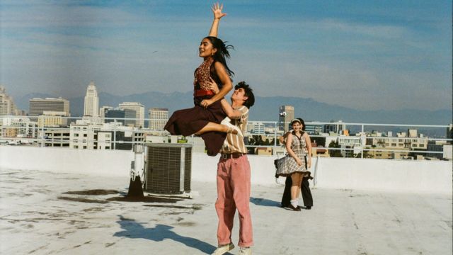on a rooftop under the downtown Los Angeles sun, a light skinned male dancer lifts a dark skinned female dancer whose arm stretches high above her head