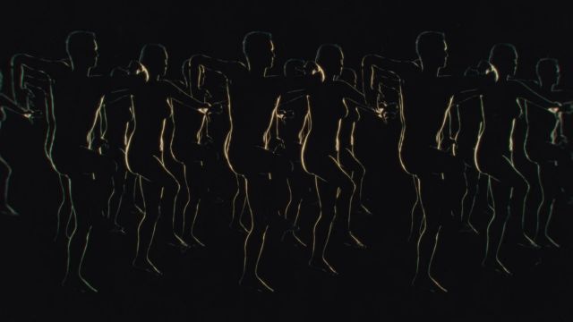 on solid black background, the silhouettes of over 20 people are illuminated just enough to show that they are marching