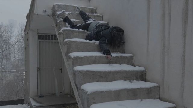 a woman lies limp on a set of snow-covered stairs, right arm outstretched; she appears lifeless