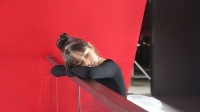 a young girl in a black leotard and white tutu rests her head on her arms, which are folded and resting on top of a glass half wall