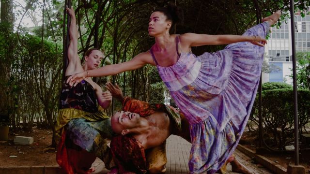 three dancers in colorful pastel colored costumes interact with a metal arbor covered in climbing plants