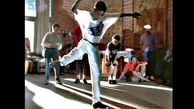 a young dark skinned boy in jeans and a white tee shirt taps as his peers look on