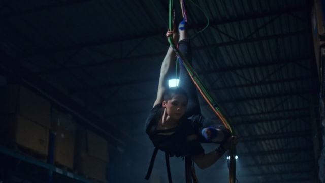 a young dancer hangs from aerial fabric in a dimly lit industrial warehouse