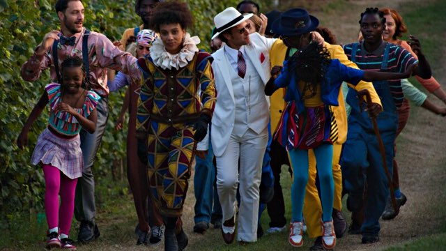 a group of people of varying ages, genders, skin colors and clothing walk and interact warmly through a vineyard