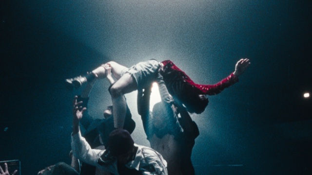 at a concert in a small club, several audience members lift up another audience member wearing a red shirt