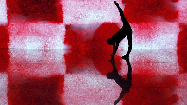 the silhouette of a dancer doing the splits in front of a bright backdrop of red and white that reflects off the floor