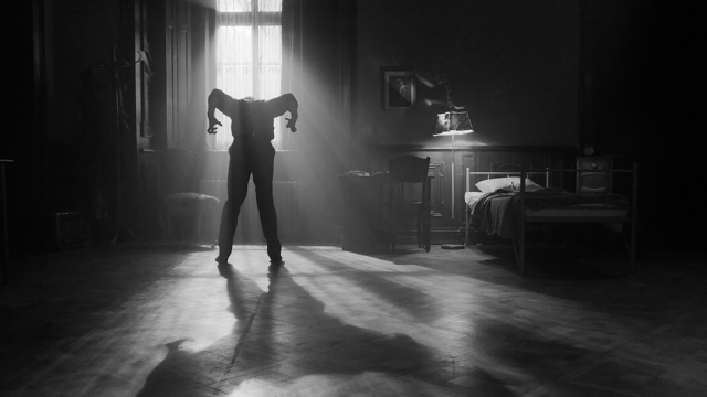 a monochrome shot of a dancer silhouetted against an open window, head down and elbows up in an insect-like position