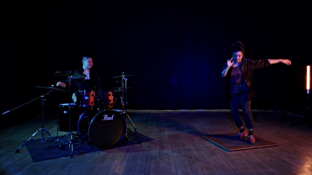 on a stage, a drummer plays a drum set and a tap dancer taps on a tap board