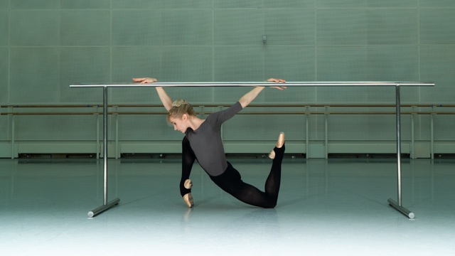 a light skinned ballerina stretches on a barre in a dance studio