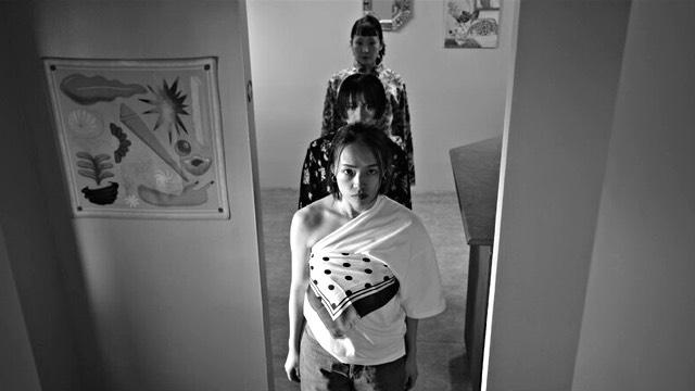 a monochrome photo of three female dancers lined up in a doorway inside a house