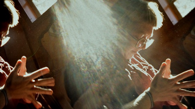 a closeup of two people with their fingers pressed together and sunlight streaming in through a window behind them