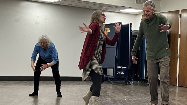 a female instructor leads two smiling older adults in a light movement class