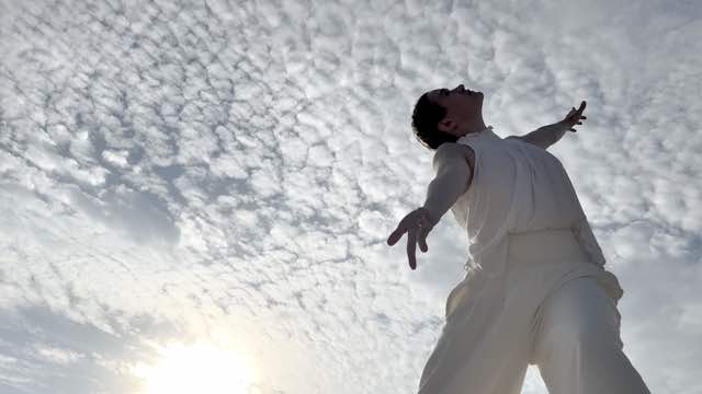 from ground level, we look up toward a sky filled with cottonball-like clouds while woman wearing all white moves gracefully