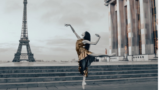a woman with long dark hair in a gold and black dress dance en pointe with the Eiffel Tower in the background